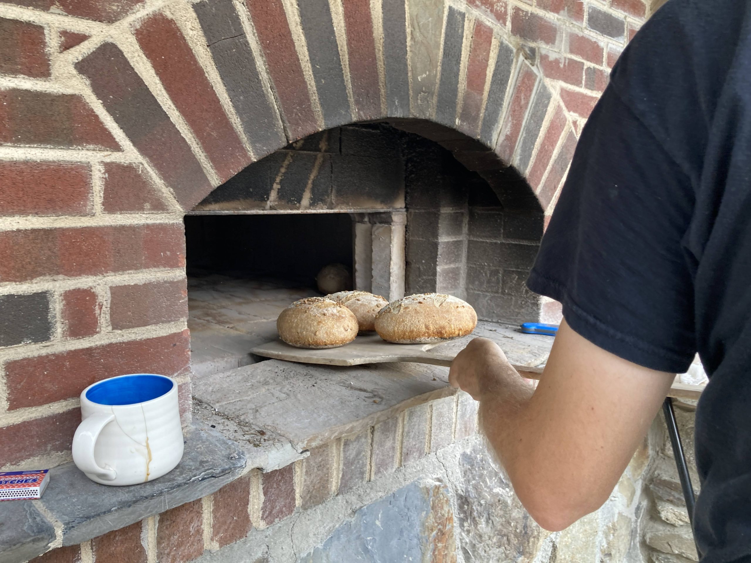 Bread loaves coming out of the outdoor brick oven